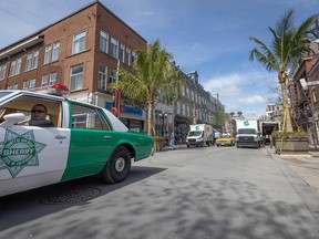 A vintage sheriff police car drives along a redecorated Ste-Catherine St. harbouring palm trees