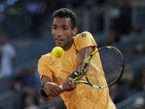 Tennis player clad in yellow top swings his racket at the ball