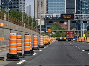 Orange cones line block off the left lane of an expressway with skyscrapers in the distance
