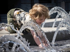 A young child reaches into a fountain from its ledge