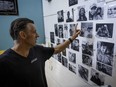 A man points to black and white photos on a wall. The photos are of unhoused Montrealers who have died.