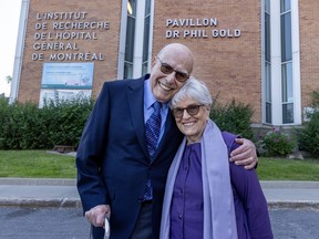 An older man and woman embrace in front of a building with the words Pavillon Dr Phil Gold