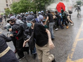 A group of masked protesters runs away from police as a cloud forms in the background