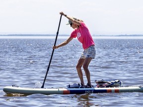 A woman paddles while standing up on a combination paddleboard kayak in a lake.