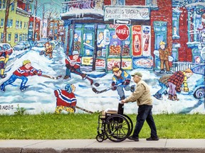 A man walks with an empty wheelchair in front of a mural depicting a winter scene.