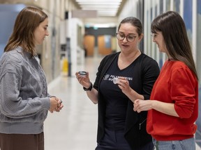Three women talk in a hallway. One is holding reusable menstrual products.