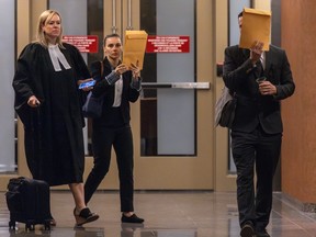 A man and a woman hold manilla envelopes in front of their faces while walking with a lawyer down a courthouse hallway.