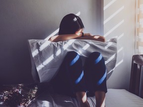 A young person sits on a bed crying into a pillow.