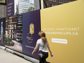 A woman walks by a temporary wall on a street advertising a residential tower construction