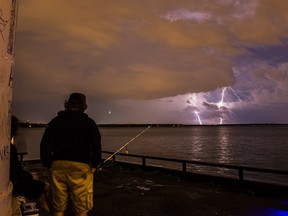 A man watches lightning strike in the distance.