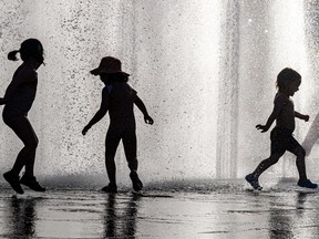 The silhouettes of three children are seen in a water fountain.