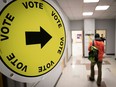 Someone arrives to vote near a yellow, circular "vote" sign pointing the way