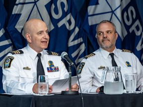 Two men in police uniforms sit at a table in front of SPVM flags