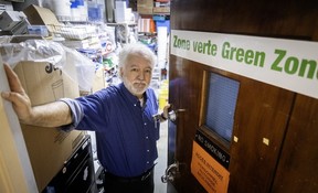 A man stands at an open door. There are piles of boxes behind him and a sign on the door that says Zone vert Green Zone
