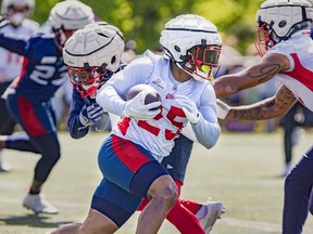 Running-back Walter Fletcher, in a white jersey and blue shorts, runs with the football during past a few Alouettes defenders during training camp.