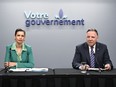 Quebec Transport Minister Geneviève Guilbault and Premier François Legault sit at a table under a sign reading Votre Gouvernement. Legault is speaking.