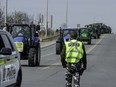 A police officer watches as farm tractors form a convoy on a rural road