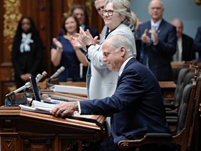 Pierre Fitzgibbon smiles as he sits at his desk in the legislature, while his colleagues stand and applaud