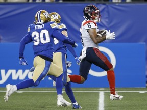 Tyson Philpot, wearing an Alouettes jersey, runs away from two Winnipeg Blue Bombers players while carrying the football on the field
