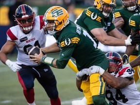 Alouettes' Mustafa Johnson, in a white jersey and blue pants, tackles Elks quarterback McLeod Bethel-Thompson, seen in the Elks' traditional dark green jersey, around the waist during game last Friday in Edmonton.
