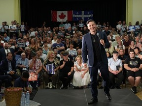 Conservative Leader Pierre Poilievre faces the camera while standing on a stage with a microphone in his left hand as the giddy crowd behind him looks on during a rally in Montreal.