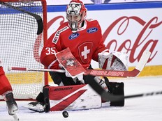 A goaltender in a Swiss hockey uniform looks at a puck near his right pad