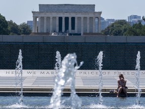 Angie Fagan, from Bassfield, Miss., cools her feet in the Rainbow Pool at the World War II Memorial, with the Lincoln Memorial behind, Friday, June 21, 2024, in Washington.