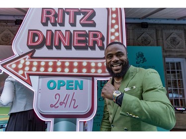 A man in a green suit poses in front of a '50s-style sign that says Ritz Diner Open 24h
