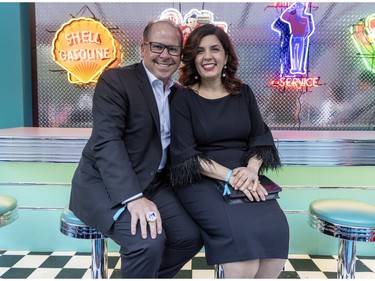 A man and woman pose at the counter of a '50s-style diner.