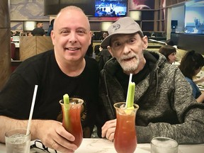 Two men pose for a photo sitting at a table with bloody Caesar drinks in front of them