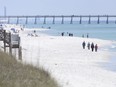 People walk along the shoreline in Navarre Beach, Fla.