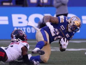 An Alouettes player grabs the legs of a Blue Bombers player falling to the turf with a football