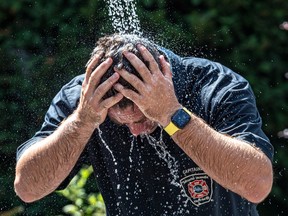 A man wearing a firefighter shirt sticks his head under falling water
