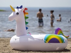 An inflatable unicorn beach toy is seen on the sand, with people in the water in the background.