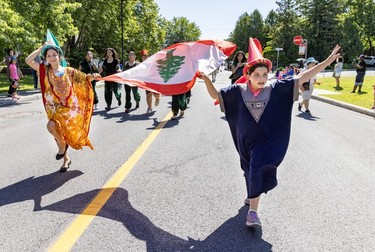 Two dancers in colourful dress hold a flag during a Canada Day parade.