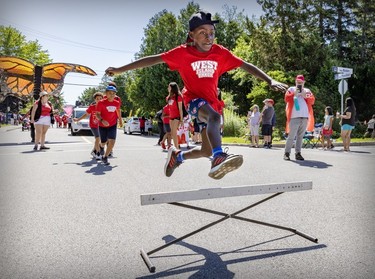 A boy jumps high over a hurdle during a Canada Day parade.