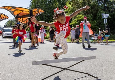 A child with Canadian flags on their head jumps over a hurdle during a Canada Day parade.