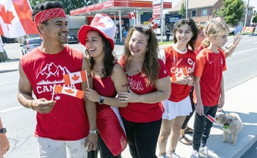 A small group of onlookers in red and white and holding flags watch a Canada Day parade.