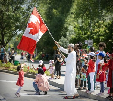 A man waves a large Canadian flag above the head of a child during a Canada Day parade.