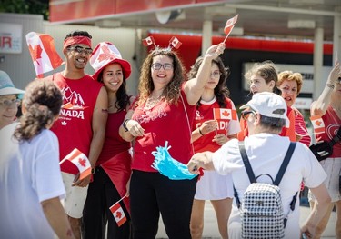 Onlookers in red and white holding small flags cheer on a Canada Day parade.