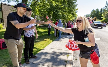 A woman smiles as she hands miniature Canadian flags to two men during a Canada Day parade.