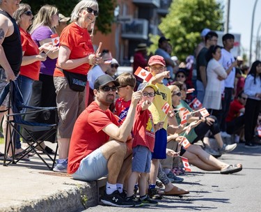 Onlookers watch a Canada Day parade while holding flags.
