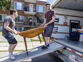 Two men hold a small table as they carry it up a ramp onto a truck
