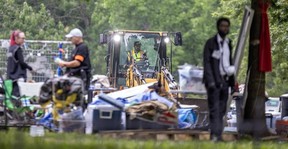 People mill about as a front-end loader prepares to clear an encampment.