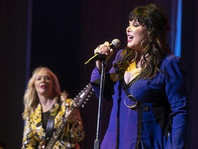 Ann Wilson sings into a microphone while Nancy Wilson plays guitar in the background