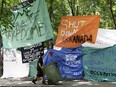 Two people push a large green waste bin on wheels beside large tarps with protest messages written on them