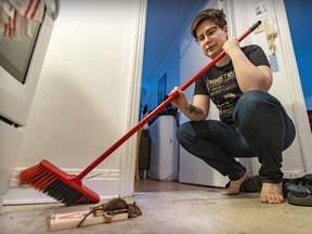 A young man with a mop looks at a dead rat caught in a spring trap.