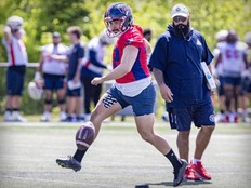 Football kicker in red practises under watchful eye of a coach.