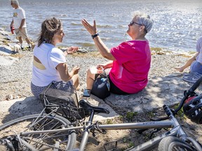 Two women talk at a beach. Their bikes are near them.