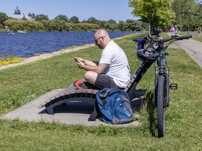 A man sits on a bench overlooking the water. He is looking at his phone and his bike is near him.